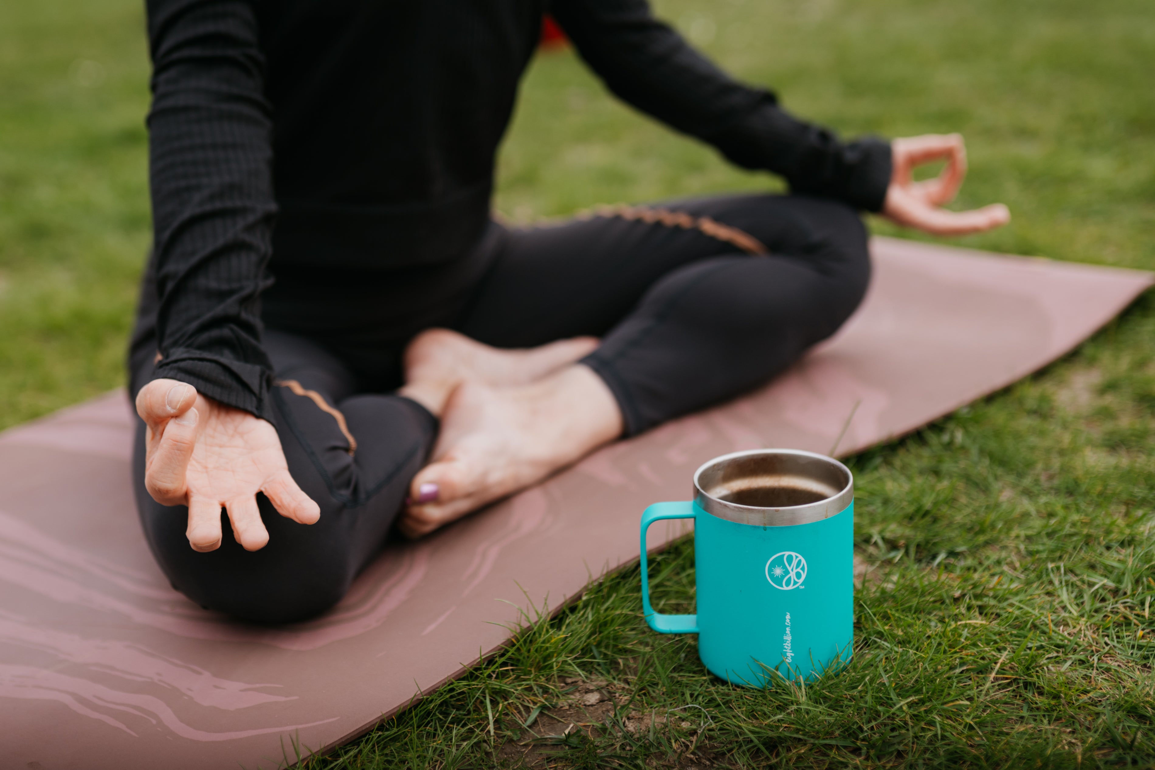 Person practicing yoga meditation outdoors on a mat with a turquoise Eight Billion coffee mug beside them. Mindful morning ritual combining wellness, calm, and functional mushroom coffee