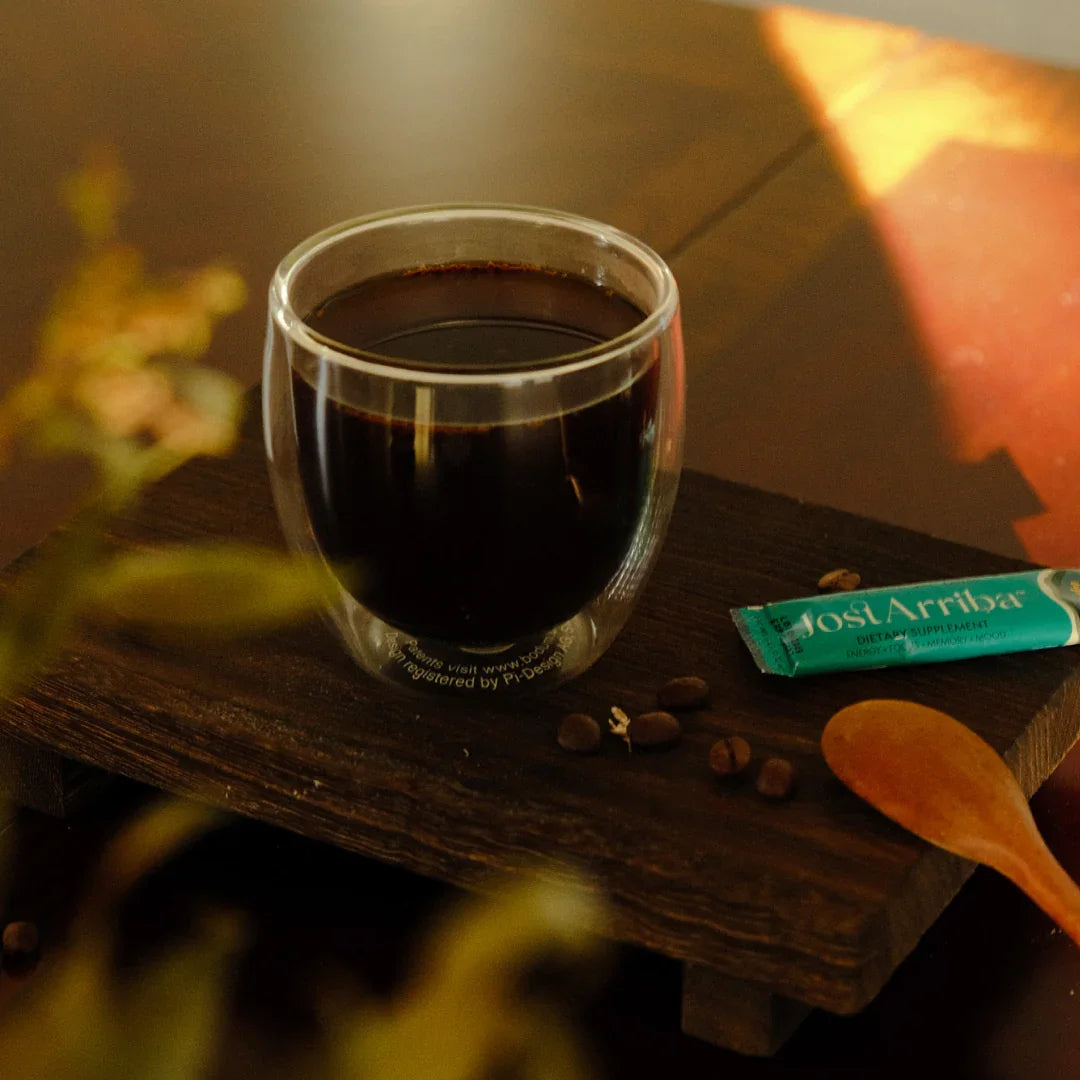 Glass cup of JostArriba adaptogenic coffee on a wooden board beside coffee beans, spoon, and sachet. Functional mushroom drink by Eight Billion made with lion’s mane, reishi, and ashwagandha for focus, mood, and energy. Warm, minimalist wellness vibe.
