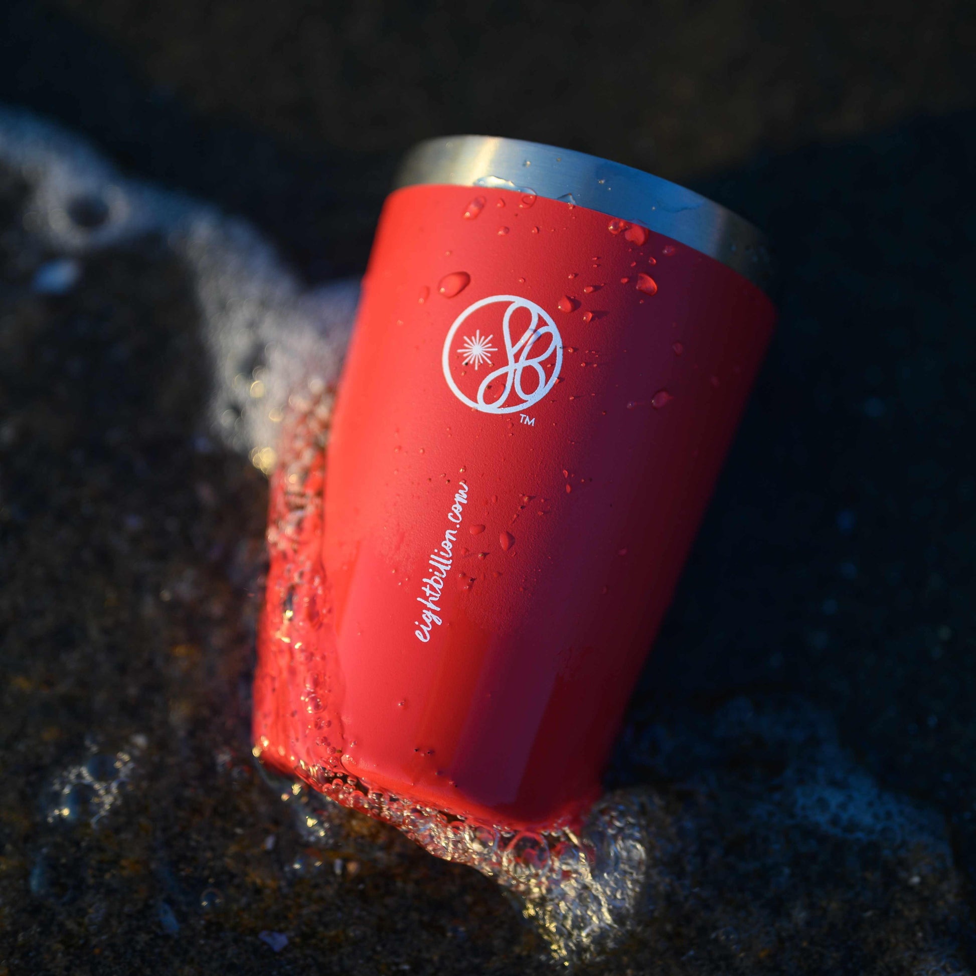 Red EightBillion reusable coffee cup with eco-friendly design resting by the ocean shore. Sustainable mushroom coffee lifestyle for wellness and reducing waste