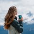 Woman holding a teal Eight Billion tumbler while overlooking a scenic mountain landscape. Enjoying JostArriba adaptogenic coffee—plant-based brain and body fuel made with functional mushrooms and botanicals. Ideal for focus, clarity, and outdoor adventures