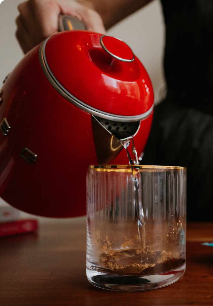 Hot water being poured from a red kettle into a glass with JostArriba mushroom coffee powder. A functional coffee alternative with adaptogens and nootropics like lion’s mane, reishi, and ashwagandha for focus, mood, and energy.