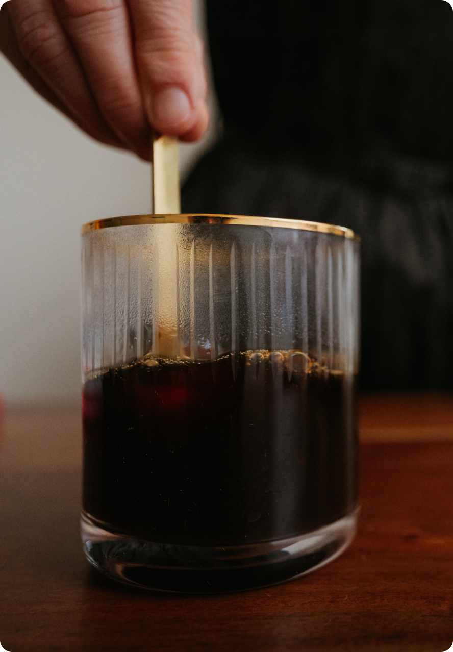 Hand stirring a glass of freshly made JostArriba mushroom coffee. A functional coffee alternative powered by adaptogens and nootropics like lion’s mane, reishi, and ashwagandha to enhance focus, mood, and brain health.