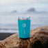 Reusable Eight Billion travel mug in turquoise, placed on driftwood by the ocean.
Eco-friendly insulated tumbler for JostArriba mushroom coffee, promoting sustainability and reducing single-use cups.