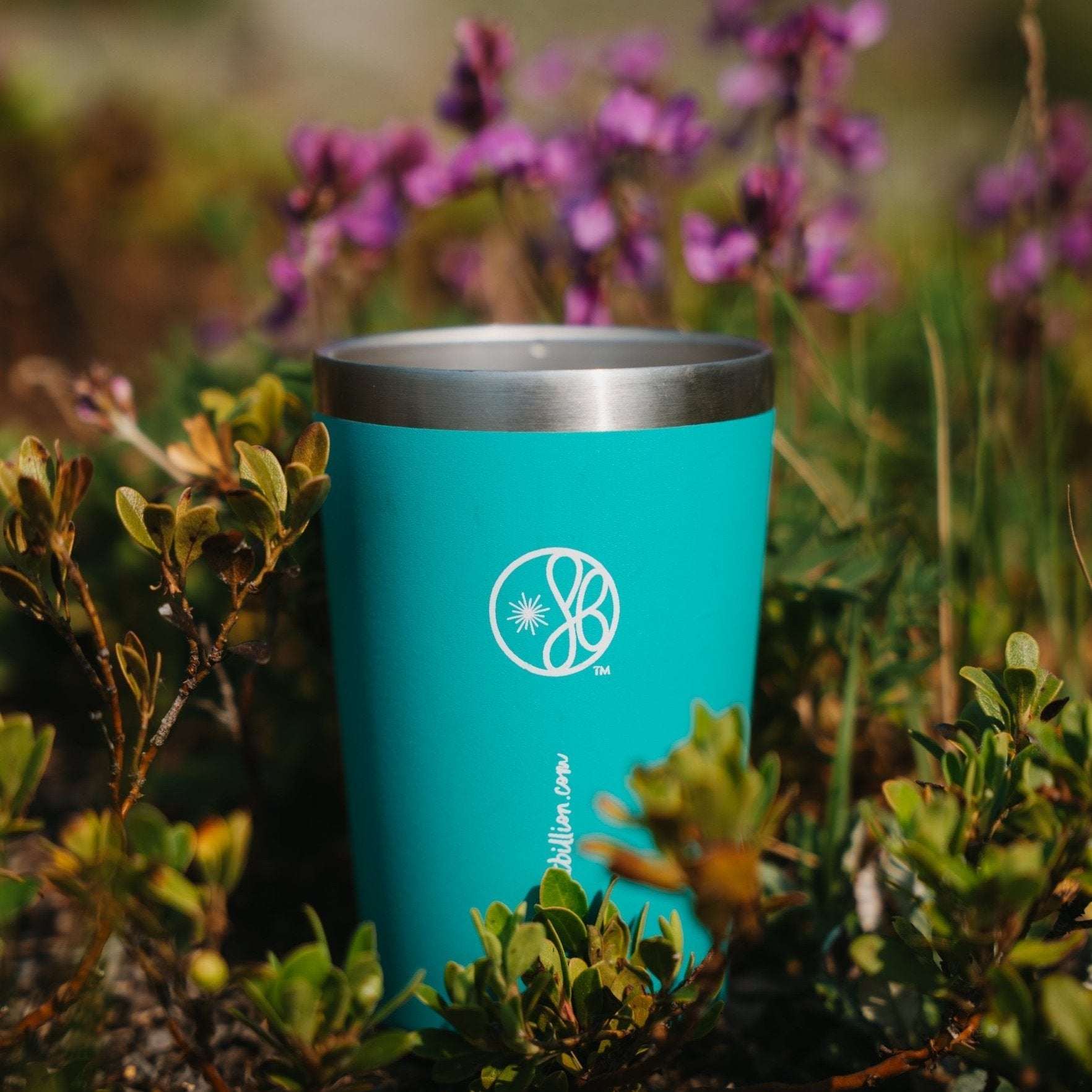 Eight Billion reusable mug with JostArriba mushroom coffee placed in nature among flowers and greenery. A brain boosting coffee alternative with adaptogens and nootropics for focus, calm energy, and mood support.
