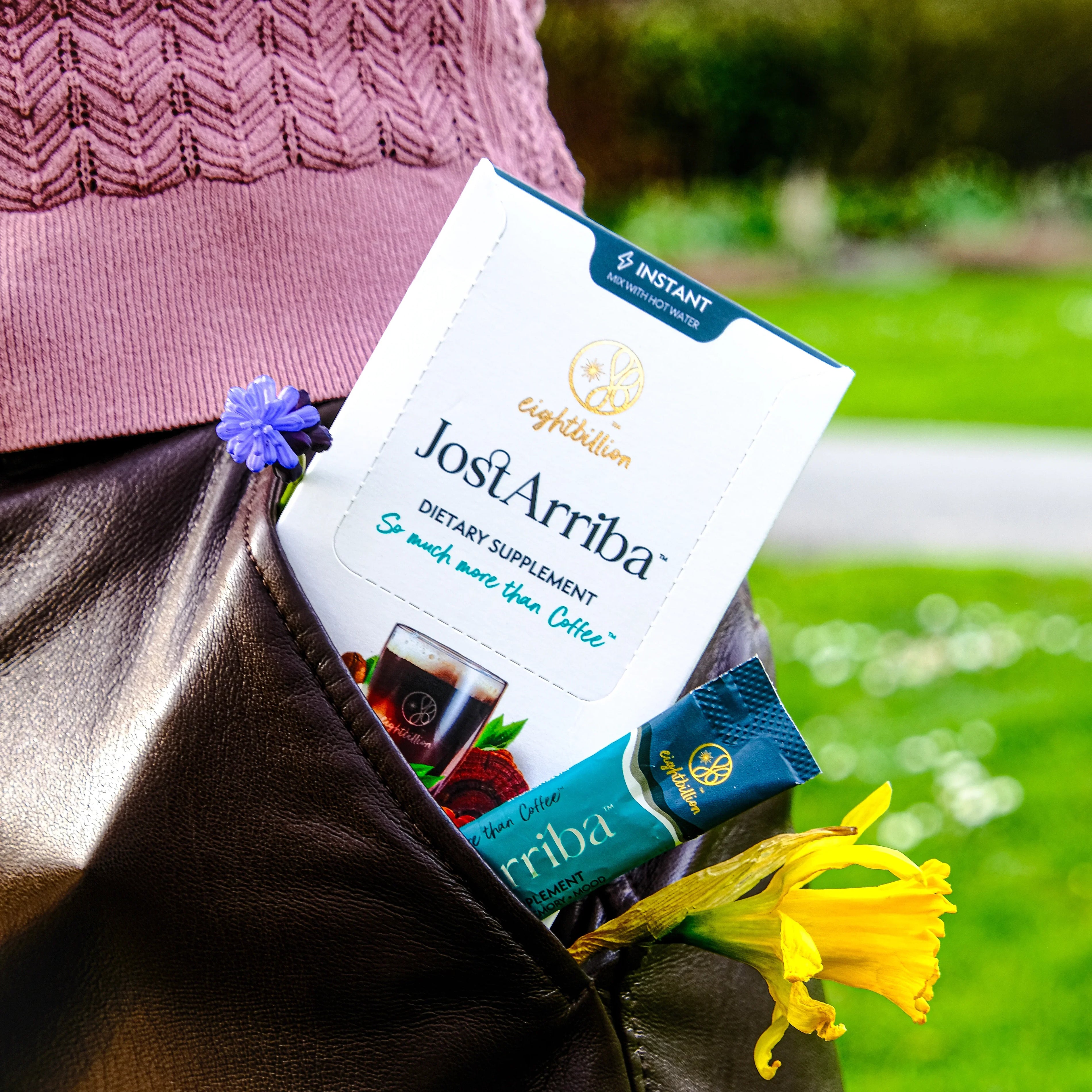JostArriba brain boosting coffee sachets and box tucked into a leather bag with spring flowers. A portable mushroom coffee alternative with adaptogens and nootropics to support focus, mood, and calm energy anywhere.
