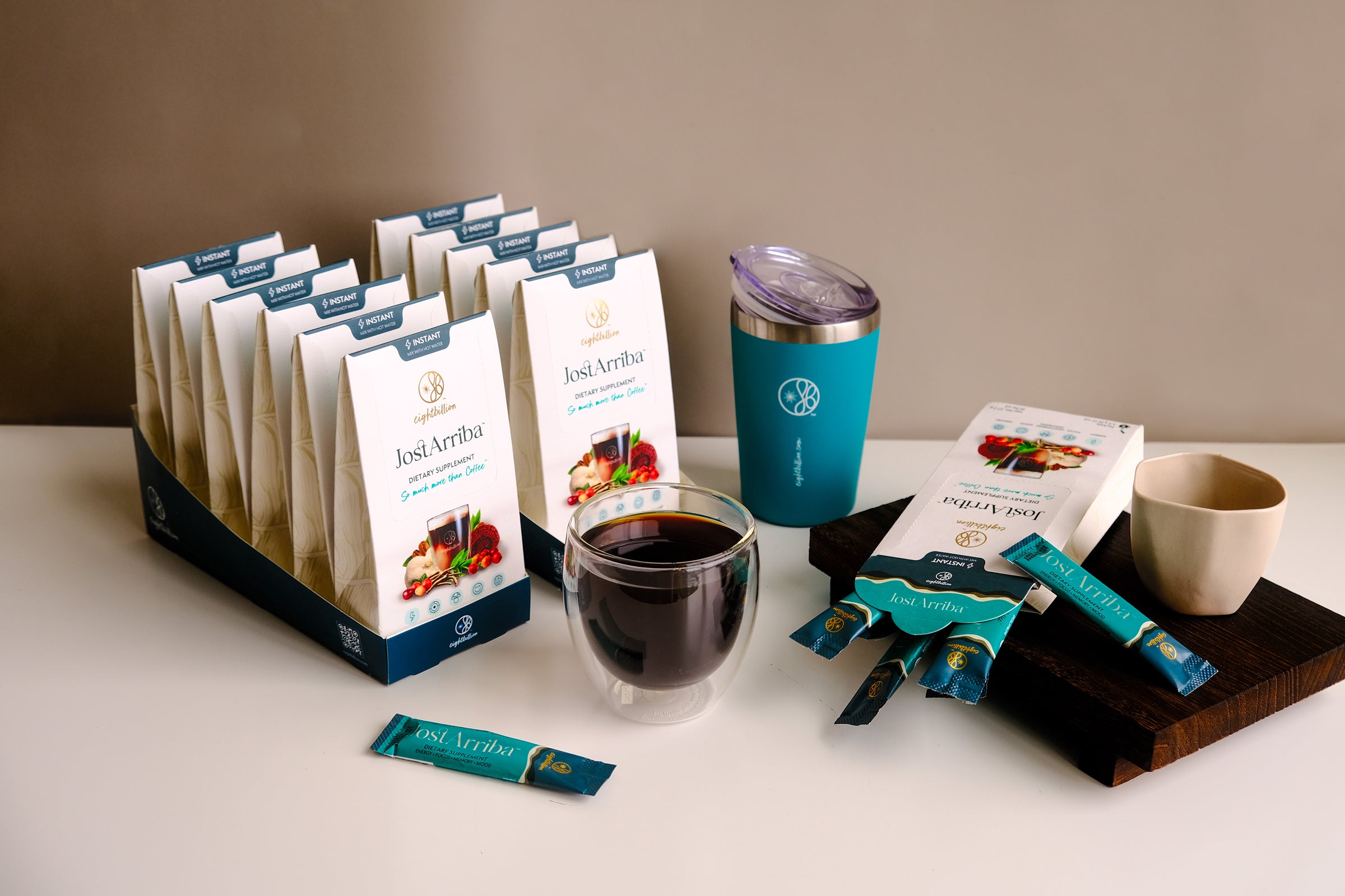 Eight Billion JostArriba wholesale display featuring boxed adaptogenic coffee sachets with lion’s mane, reishi, and ashwagandha. Includes retail-ready packaging, branded teal tumbler, and glass cup of functional mushroom nootropic drink—ideal for wellness retailers, cafés, and health food stores.